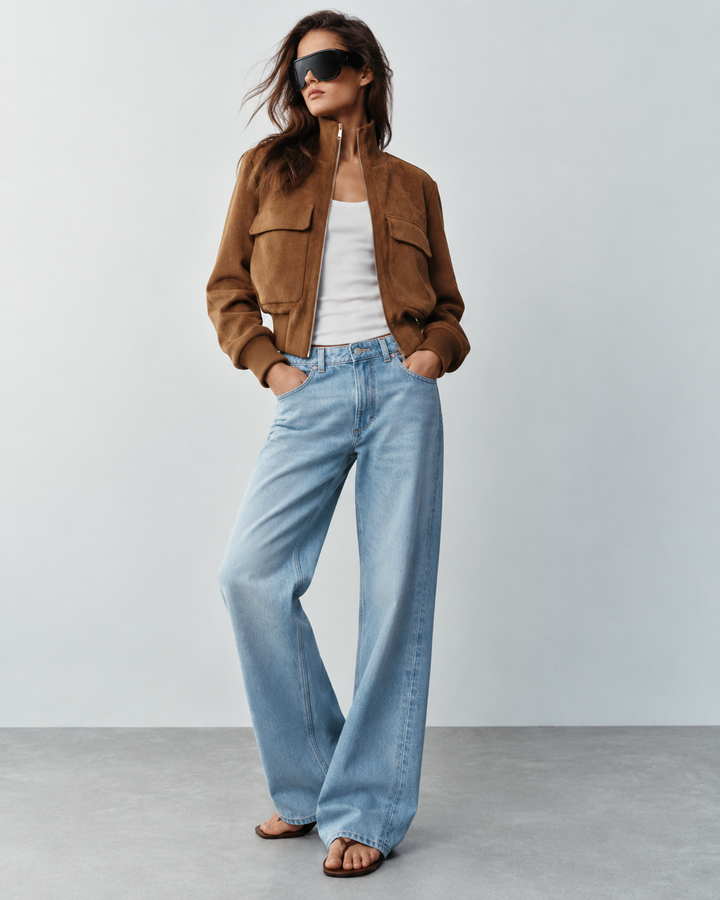 Tan suede cropped bomber jacket worn with light blue wide-leg jeans, full-length front view