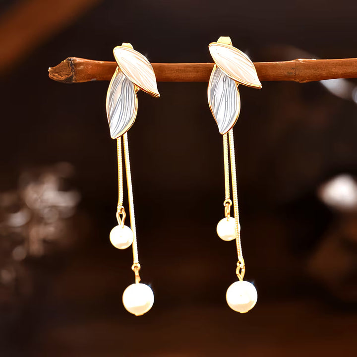 Long pearl leaf earrings laid flat against a light background
