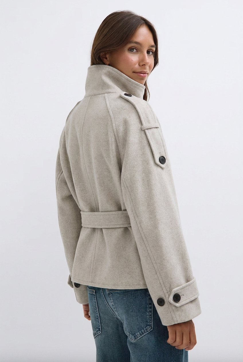 Side view of cream wool trench jacket showing funnel collar and buttoned cuff tabs
