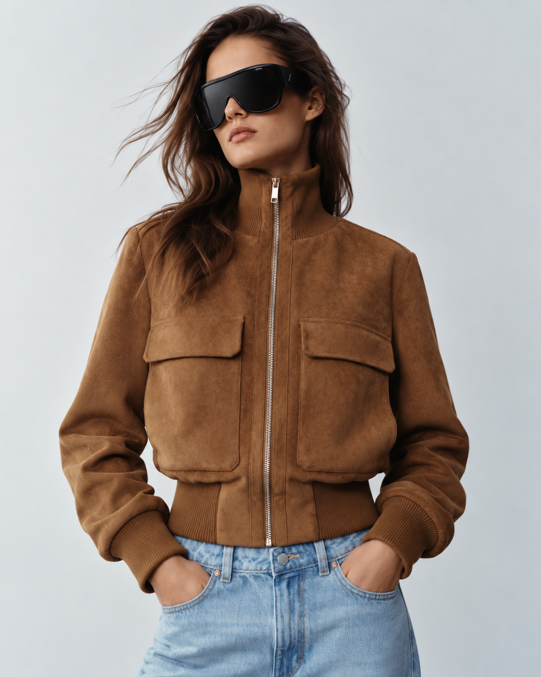 Light brown suede bomber jacket close-up showing gold zip front and two chest flap pockets