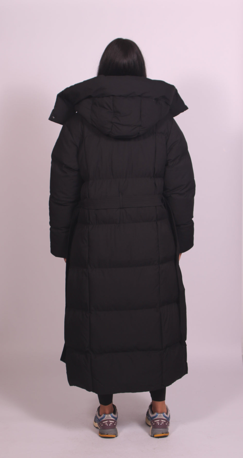 Back view of black maxi puffer coat showing detachable hood, quilted panels and back belt