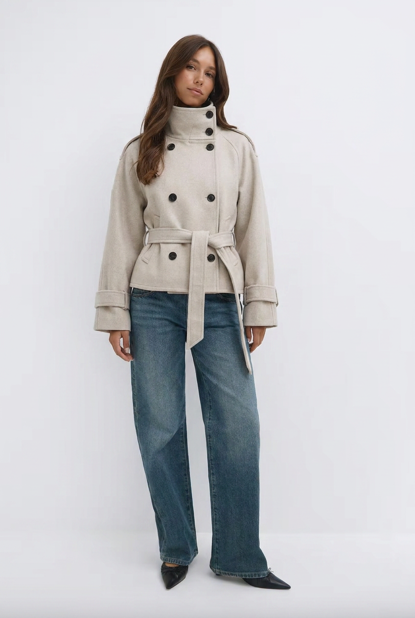 Woman wearing beige Safron short trench coat with belt, styled with blue wide leg jeans