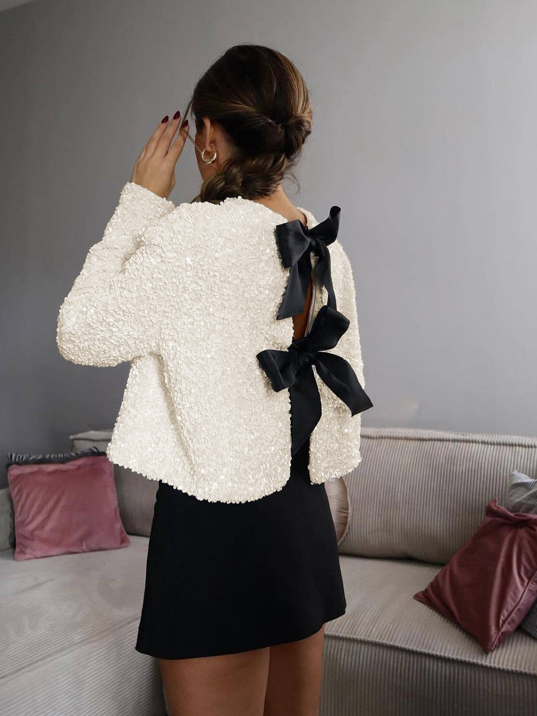 Back view of a woman wearing the cream bow detail jacket with a black mini skirt