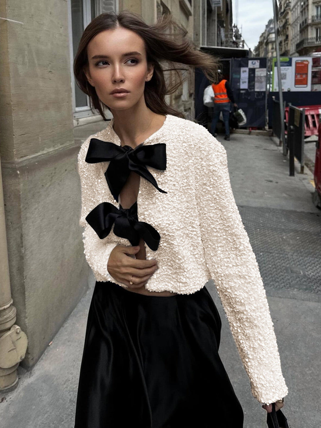 Model on a street in the white sequinned bow jacket with a black satin skirt