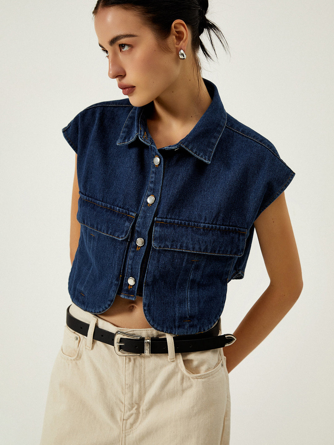 Side profile of women's denim collared vest styled with black belt and trousers