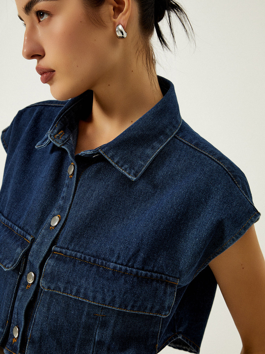 Close-up of turn-down collar, silver buttons and chest patch pocket on denim vest