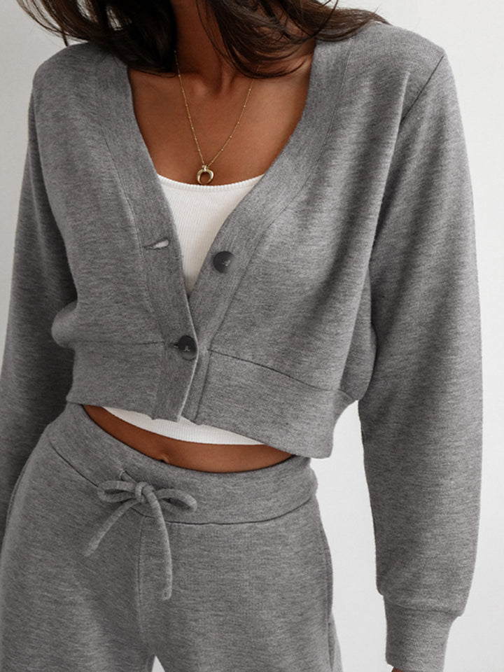 Close-up of grey cropped button cardigan jacket worn over a white top with gold necklace