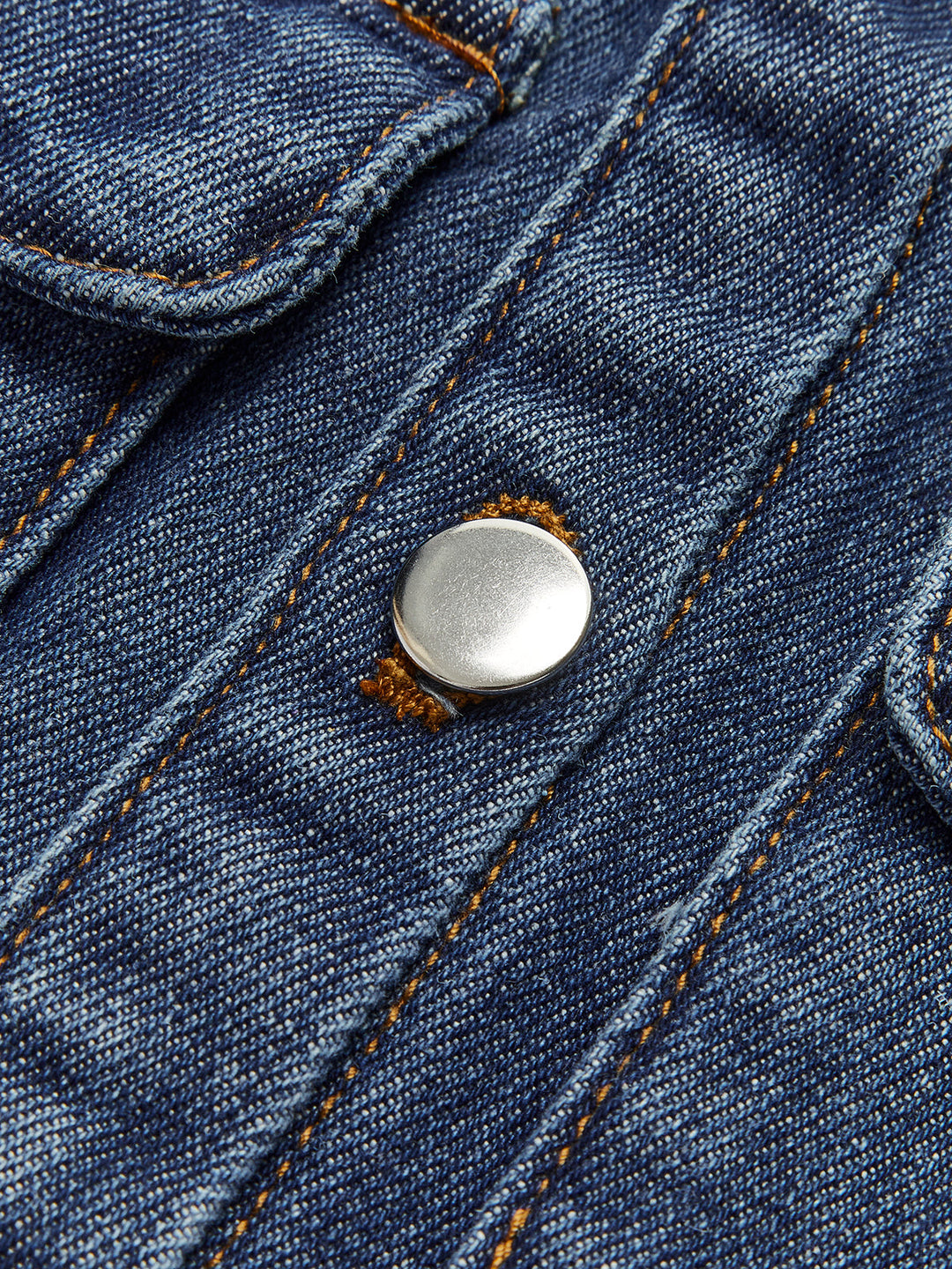 Macro of silver shank button and orange topstitching on indigo denim vest