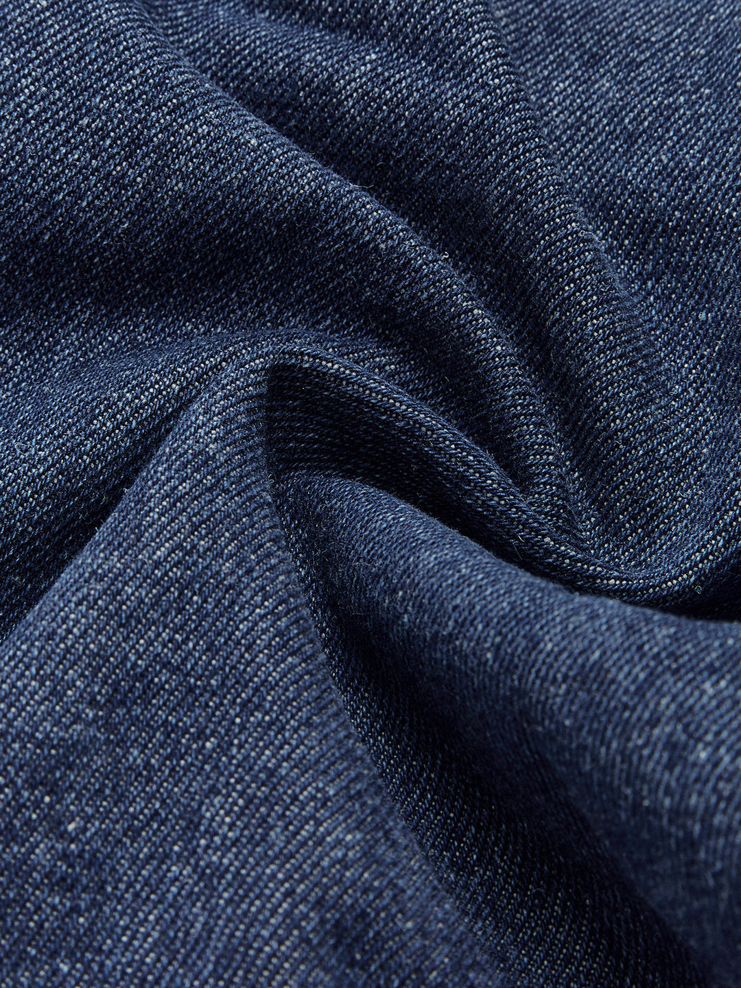 Macro of draped dark indigo denim fabric used for the collared pocket vest
