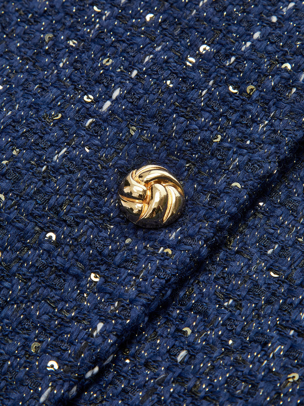 Macro of gold swirl button on navy sequin-flecked tweed vest