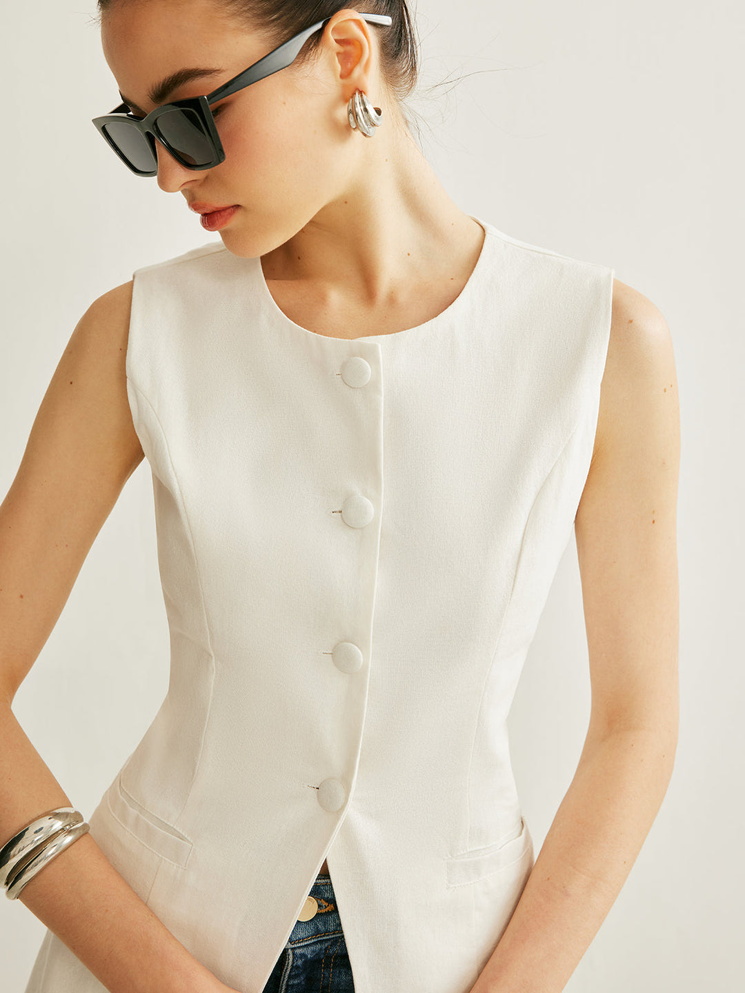 Close view of the round neckline and tonal button placket on the white linen vest