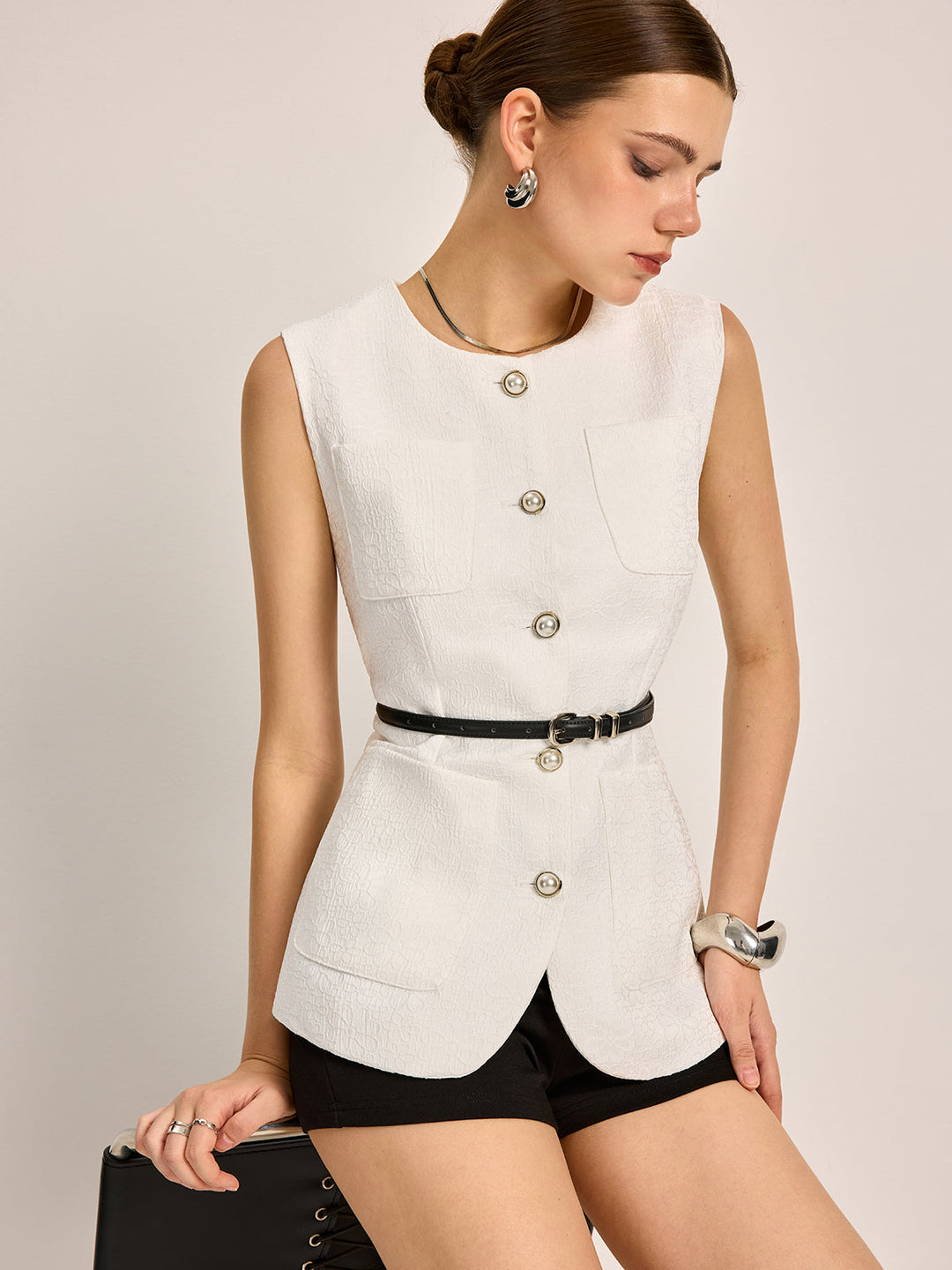 White textured sleeveless vest with silver buttons worn with a thin black belt