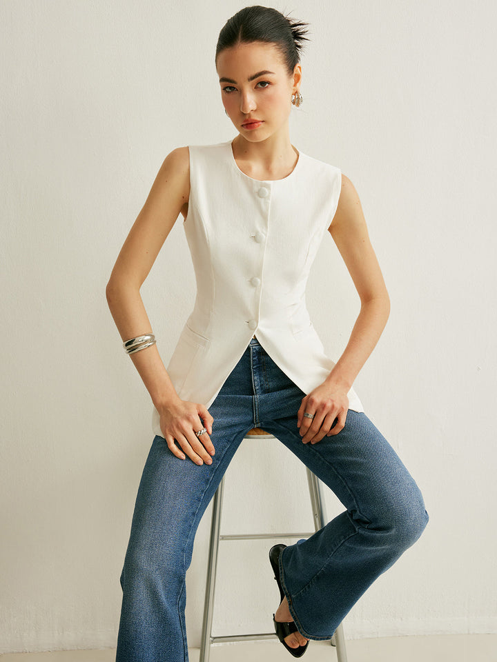 Model seated on a stool in the white button-front sleeveless vest and flared denim