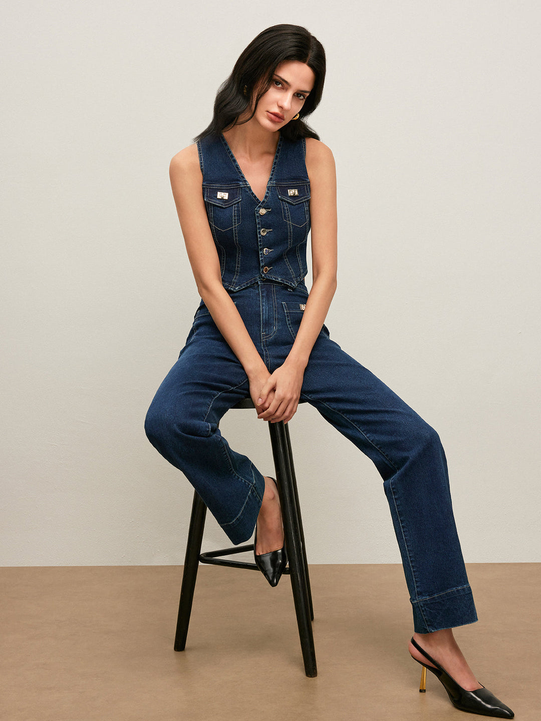 Model seated on a stool in cropped denim vest and matching blue jeans