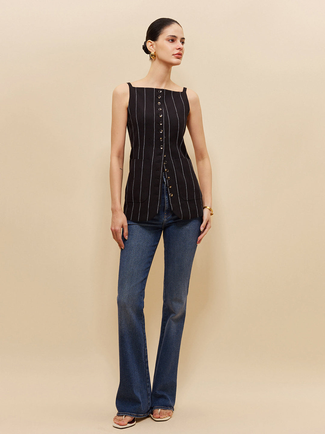Volledig model in zwart gestreept lang vest op flared jeans en witte sandalen