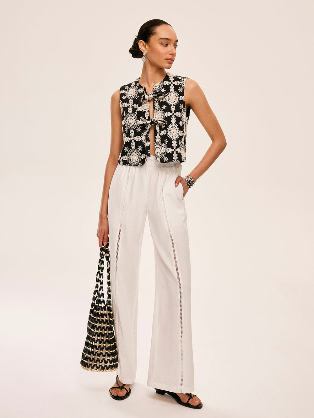 Full-length look: embroidered sleeveless cotton vest, white palazzo pants and a beaded handbag