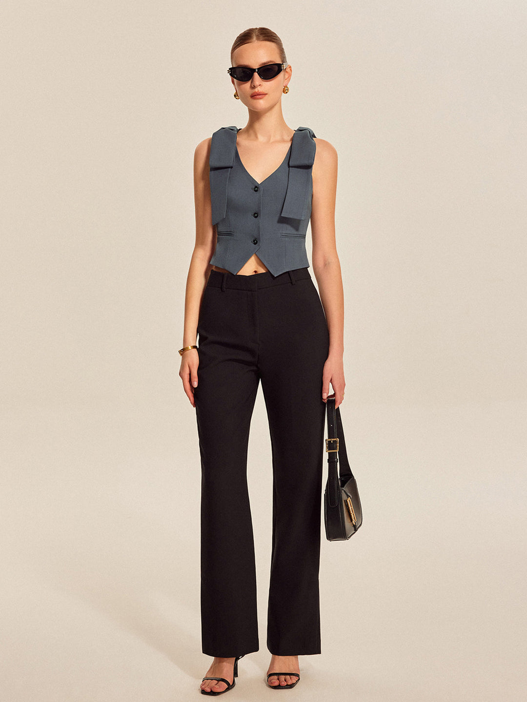 Full-length look of grey-blue cropped bow vest with black trousers and bag