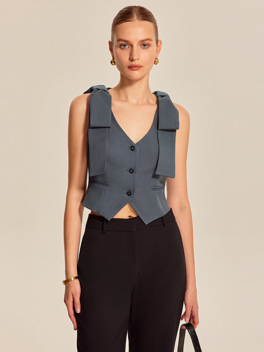 Front view of tailored bow shoulder vest with pointed hem and three dark buttons