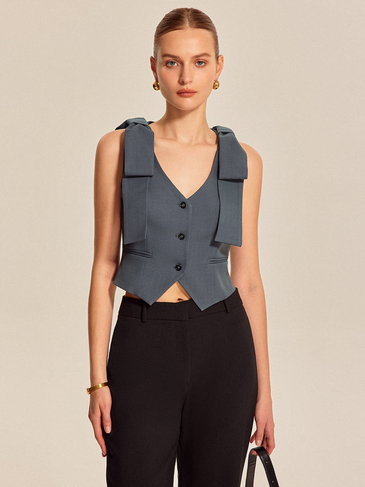 Front view of tailored bow shoulder vest with pointed hem and three dark buttons