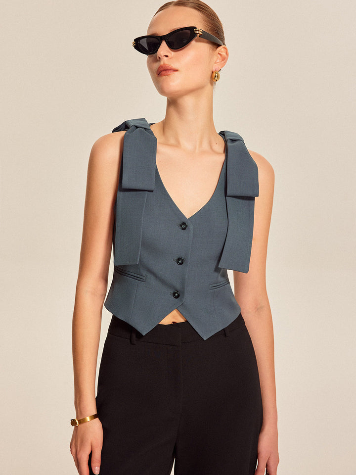Model in sunglasses wearing slate blue bow vest, close waist-up styling shot