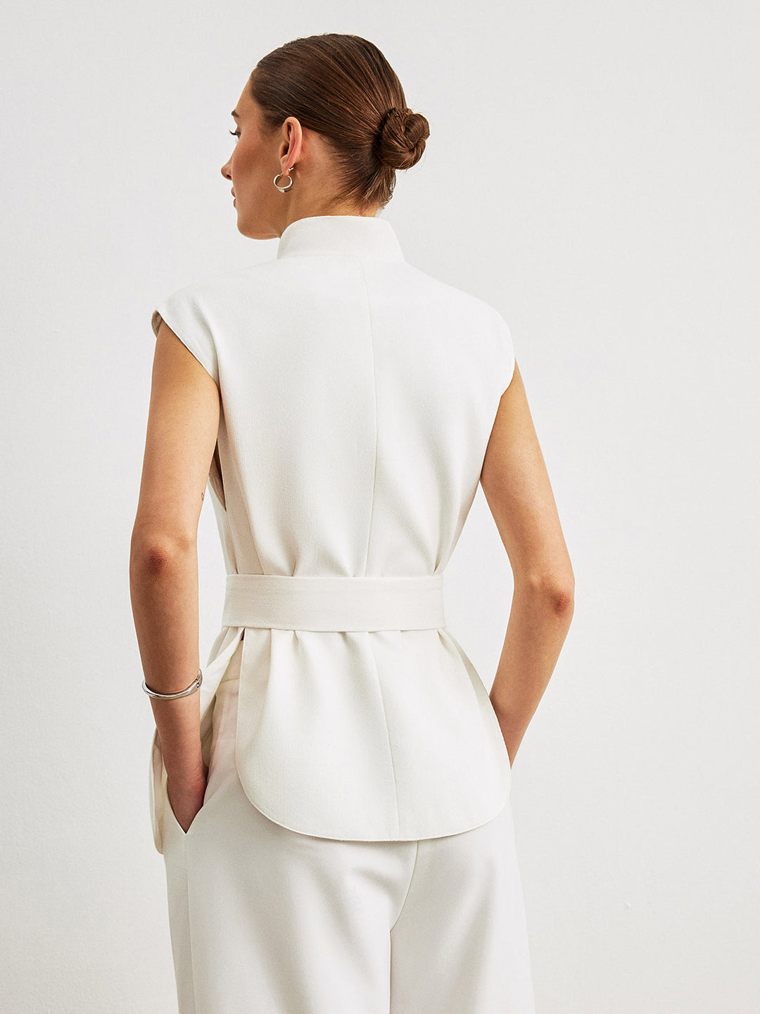 Back view of white sleeveless peplum top with belt tied at the waist