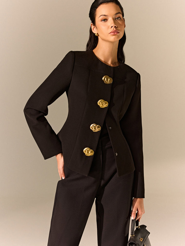 Woman in a black collarless tailored blazer with oversized gold sculptural buttons and matching trousers
