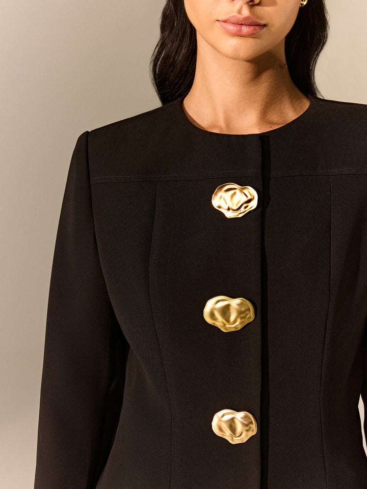 Close-up of the hammered gold buttons and collarless neckline on a black tailored blazer