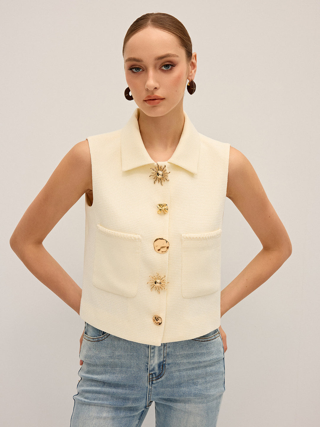 Front view of the irregular metal button vest with hands at the sides and drop earrings