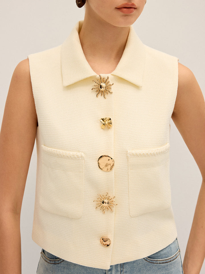 Close-up of the mismatched sculptural gold buttons and patch pockets on the cream vest