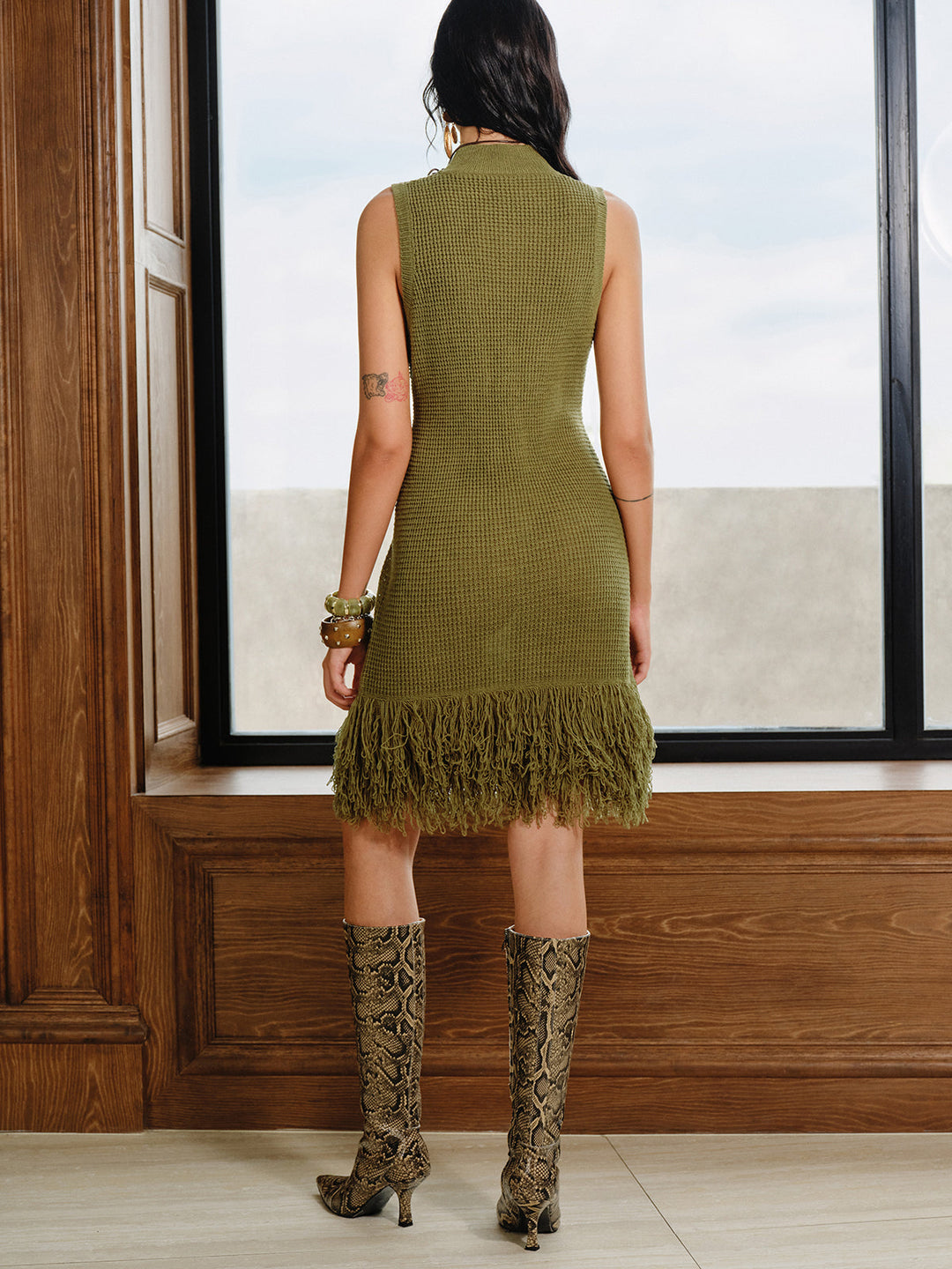 Back view of the olive green sleeveless knit dress with fringe hem and leopard boots