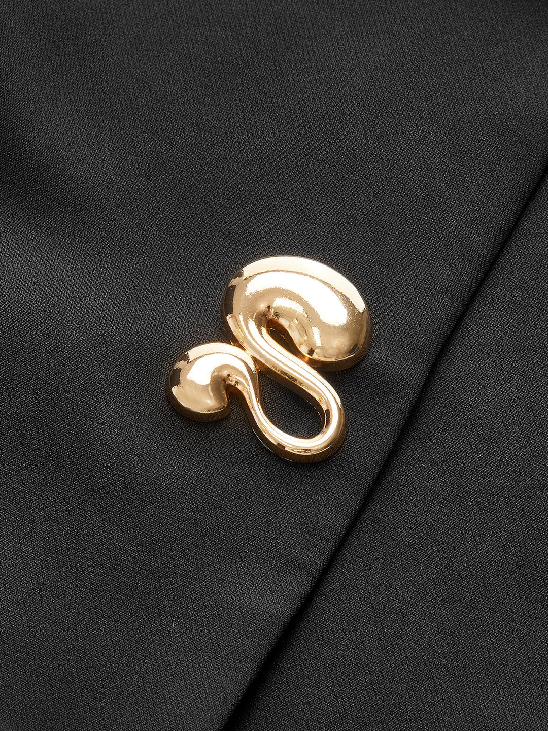 Macro of the polished gold swirl button detail on the black cap sleeve vest