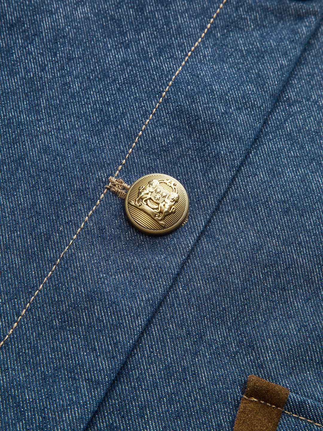 Close-up of engraved gold crest button and contrast stitching on navy denim jacket