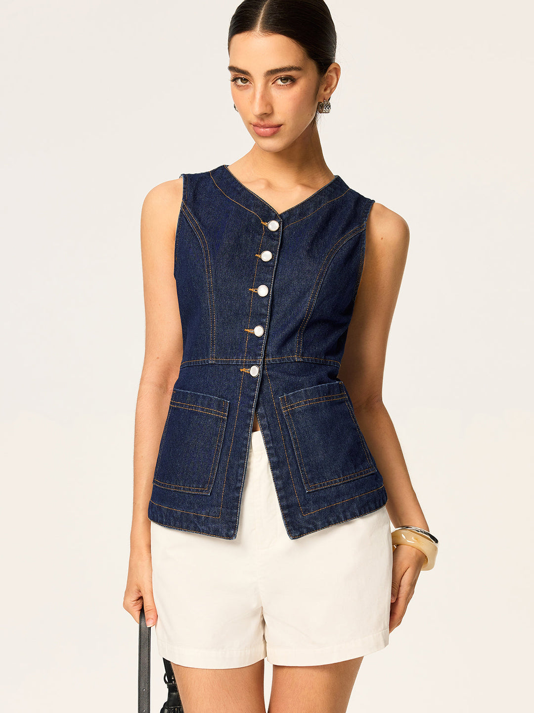 Model in sleeveless denim vest with patch pockets and white shell buttons