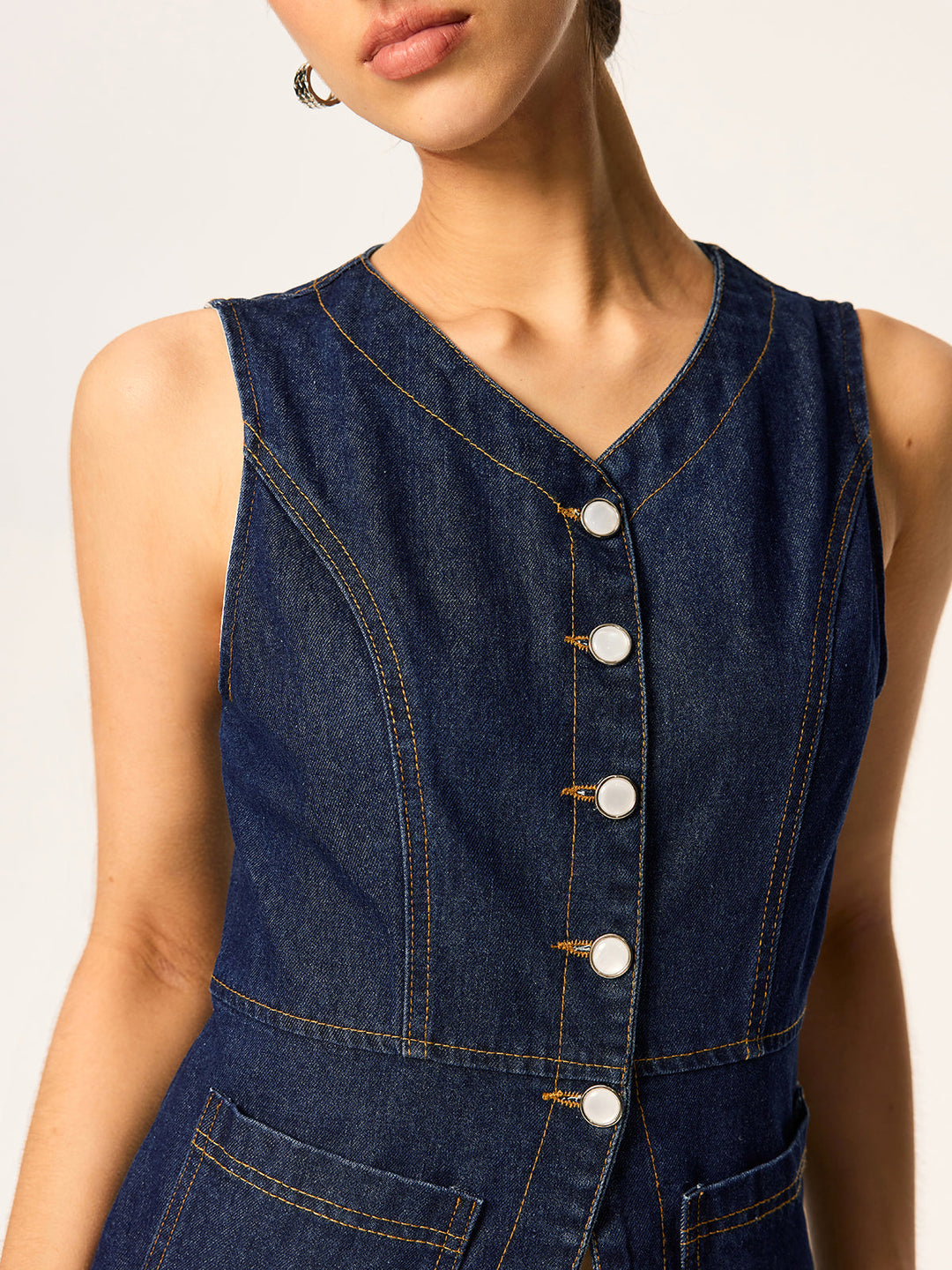 Close-up of white shell buttons down the front of a slim denim vest