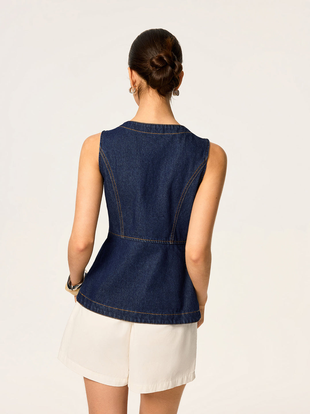 Back view of fitted denim sleeveless vest with waist seams and white shorts
