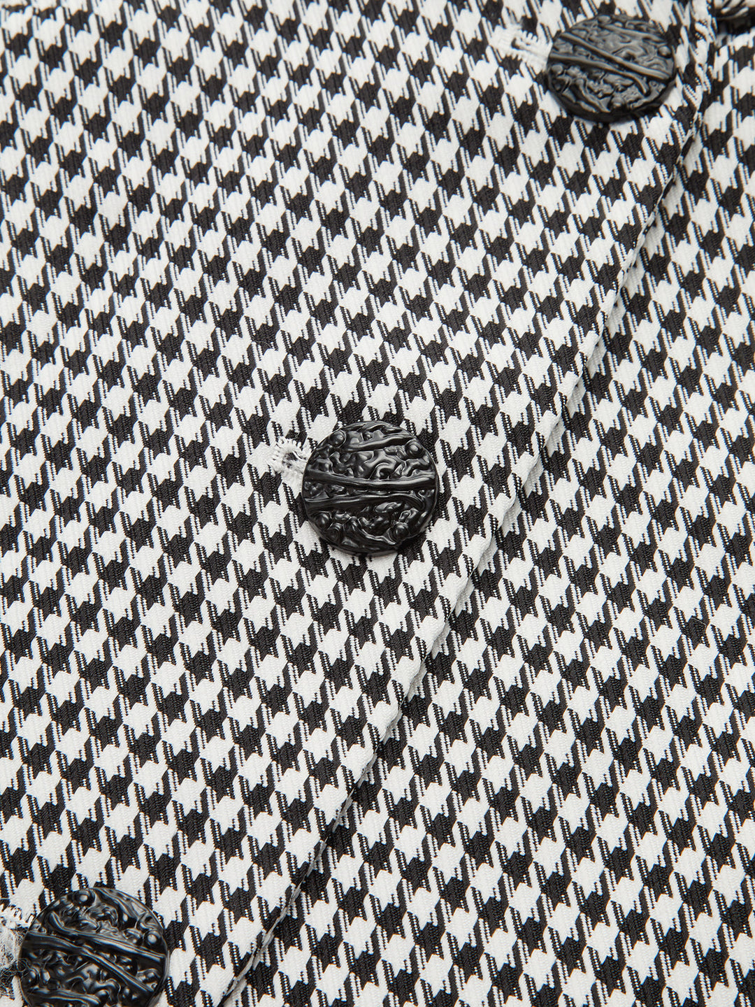 Close-up of the gold oval buckle and woven black buttons on the houndstooth vest