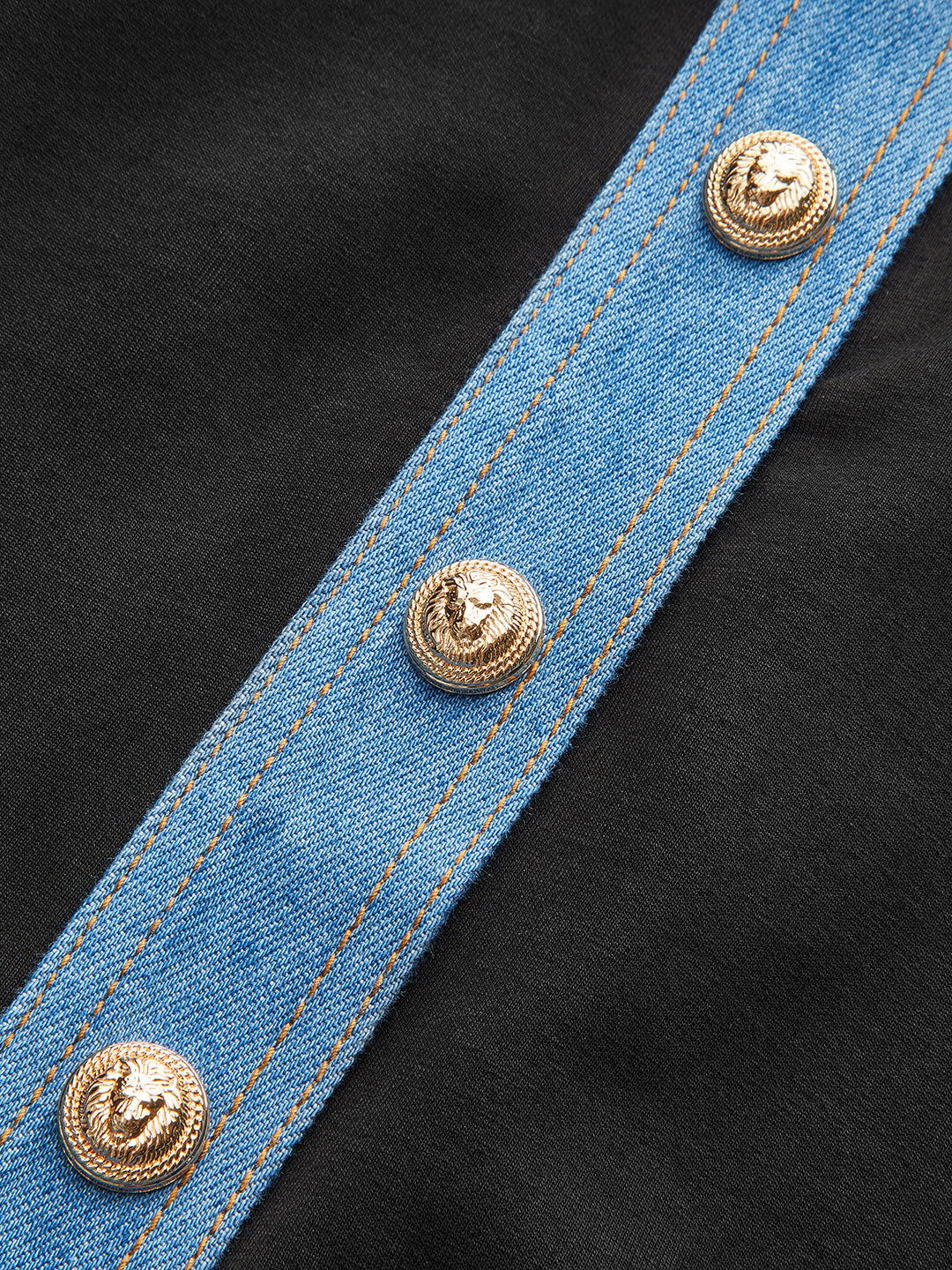 Close-up of the gold lion buttons on the blue denim placket over black fabric