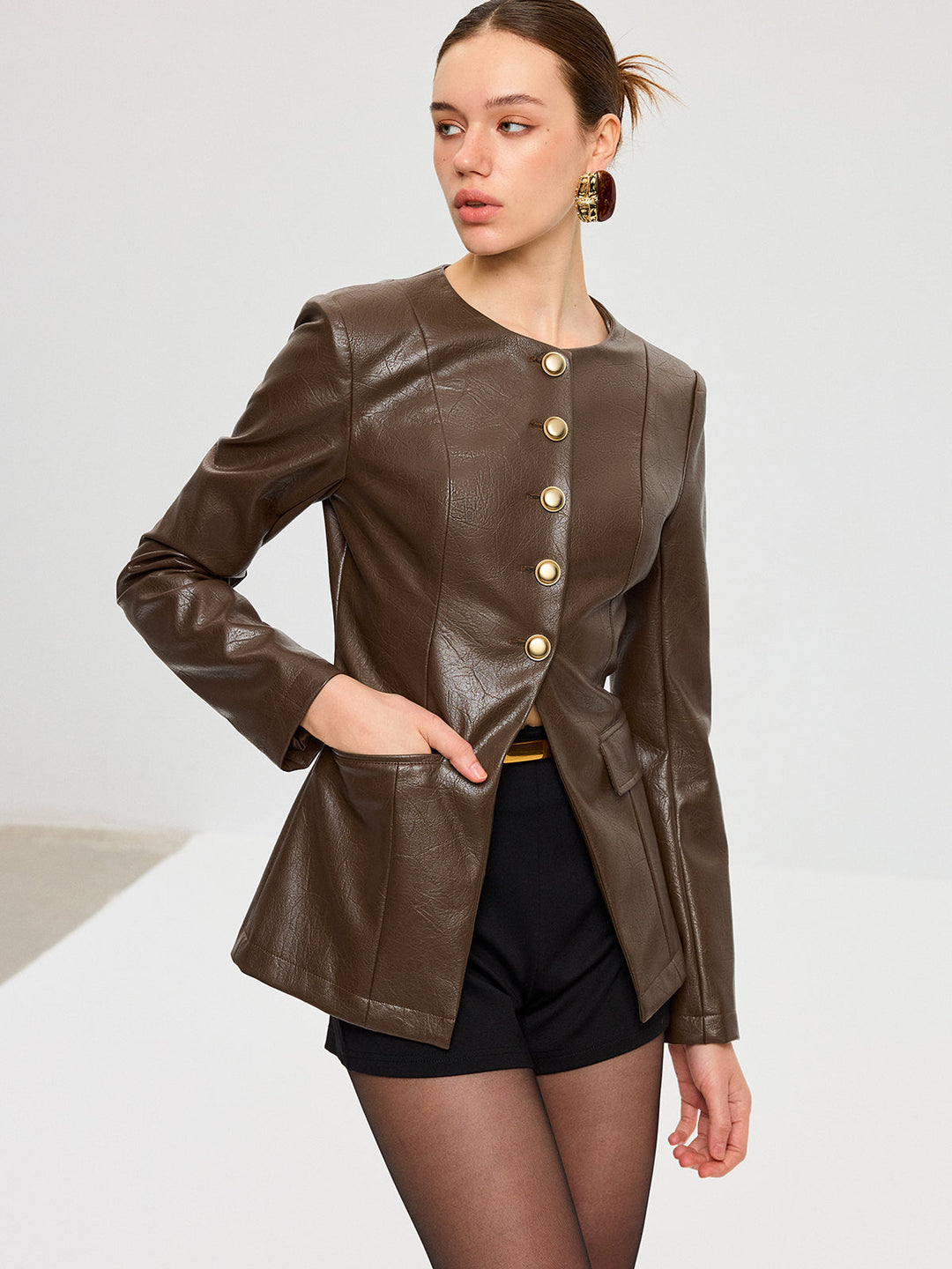 Model with hand in pocket wearing fitted dark brown PU leather jacket over black shorts