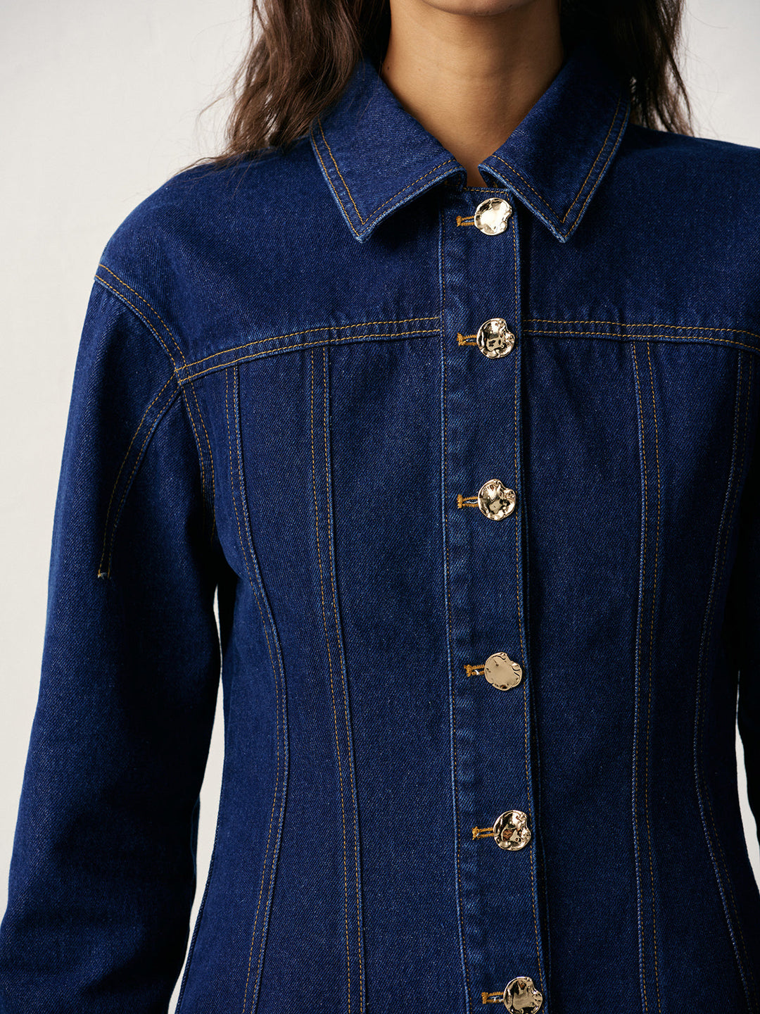 Detail of engraved gold metal buttons running down the front of a blue denim jacket