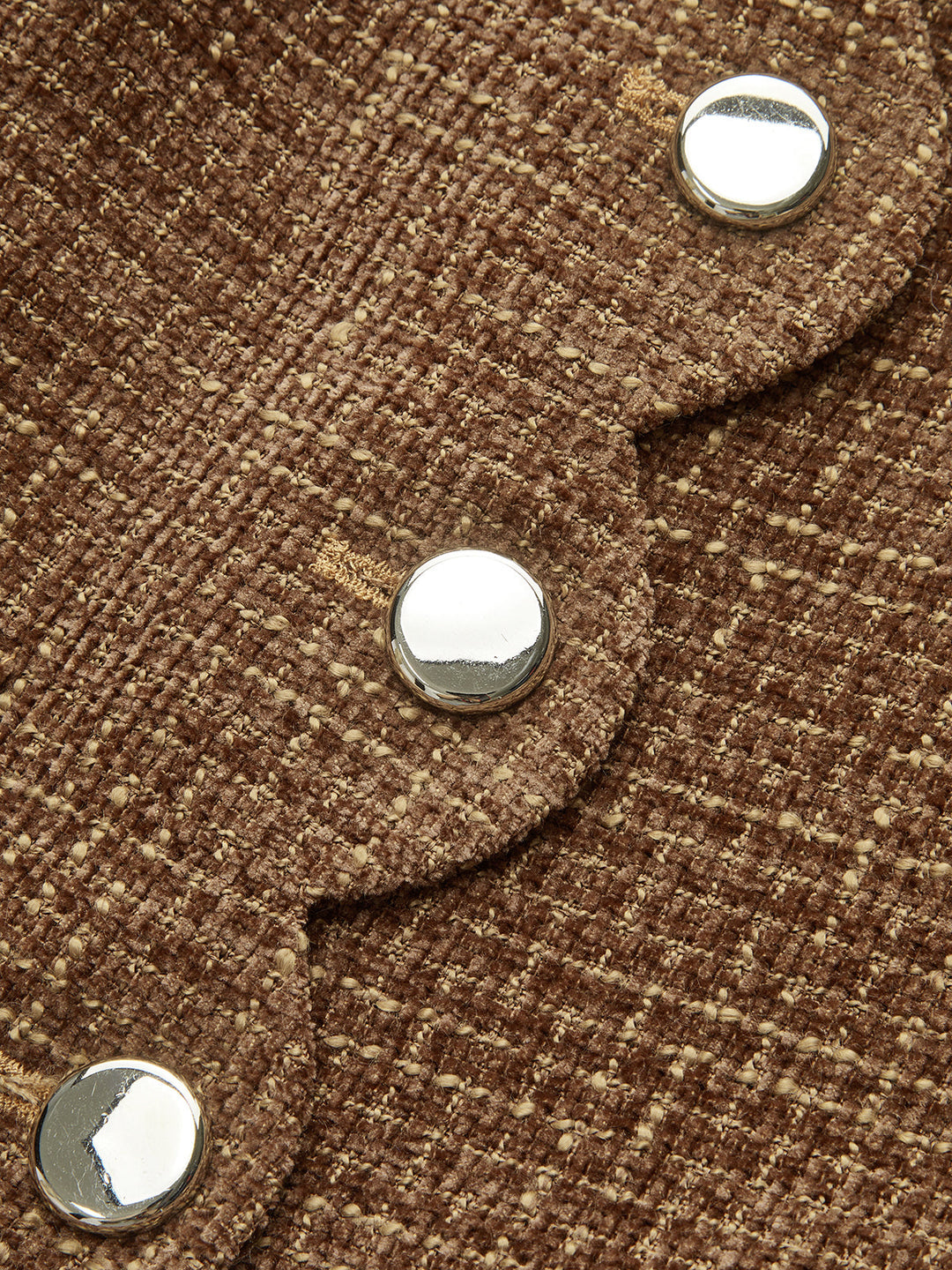 Close-up of domed silver buttons along the scalloped edge of a tweed jacket