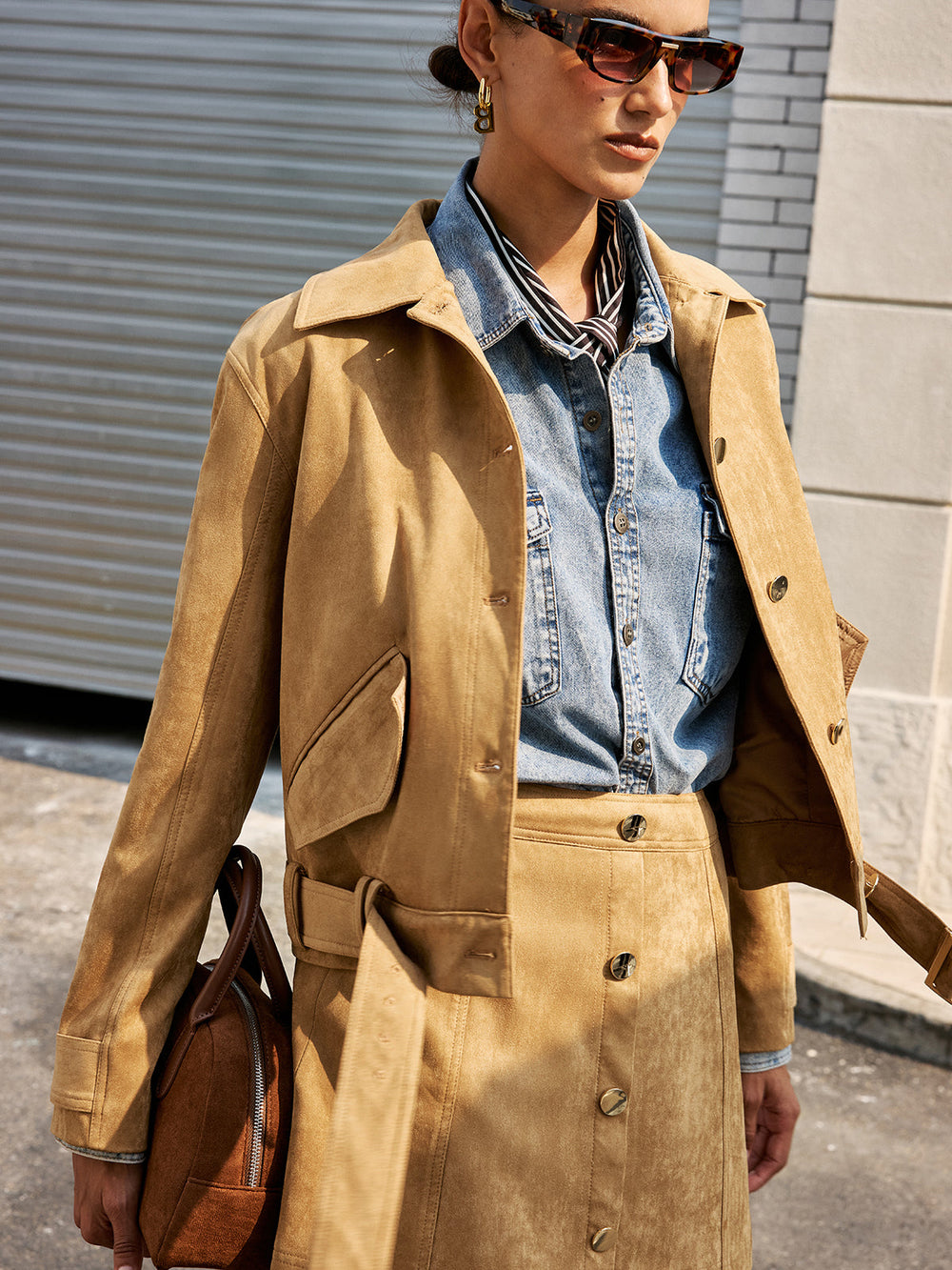 Model in the tan suede jacket over a denim shirt, carrying a brown leather bag