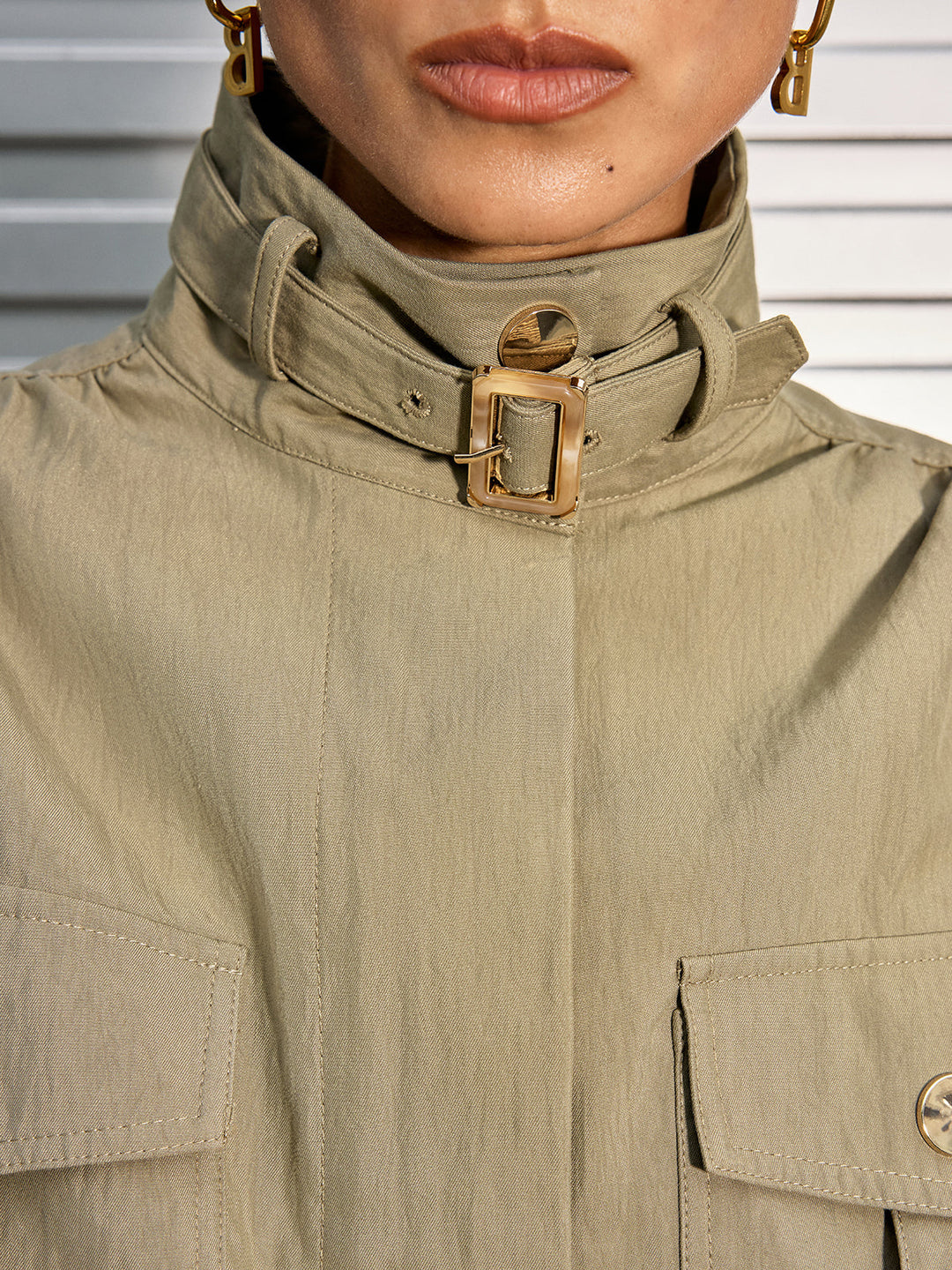 Close-up of the gold buckle strap on the high stand collar of an olive cotton blend jacket