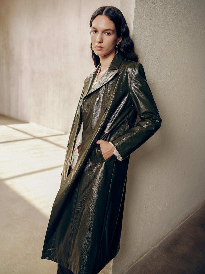 Side pose with hands in pockets showing the long line of the green patent trench coat