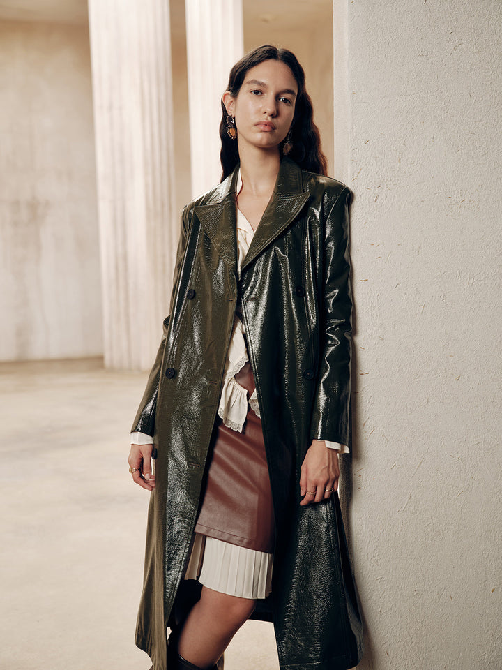 Model walking in the dark green patent faux leather coat over a leather mini skirt and boots