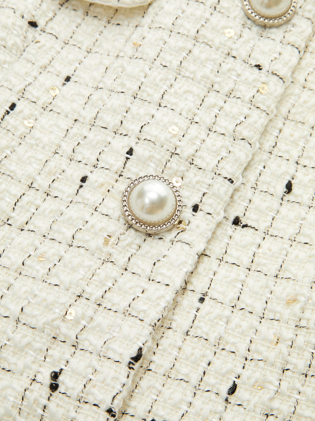Close-up of the pearl button and sequin flecked ivory tweed weave on the cropped jacket