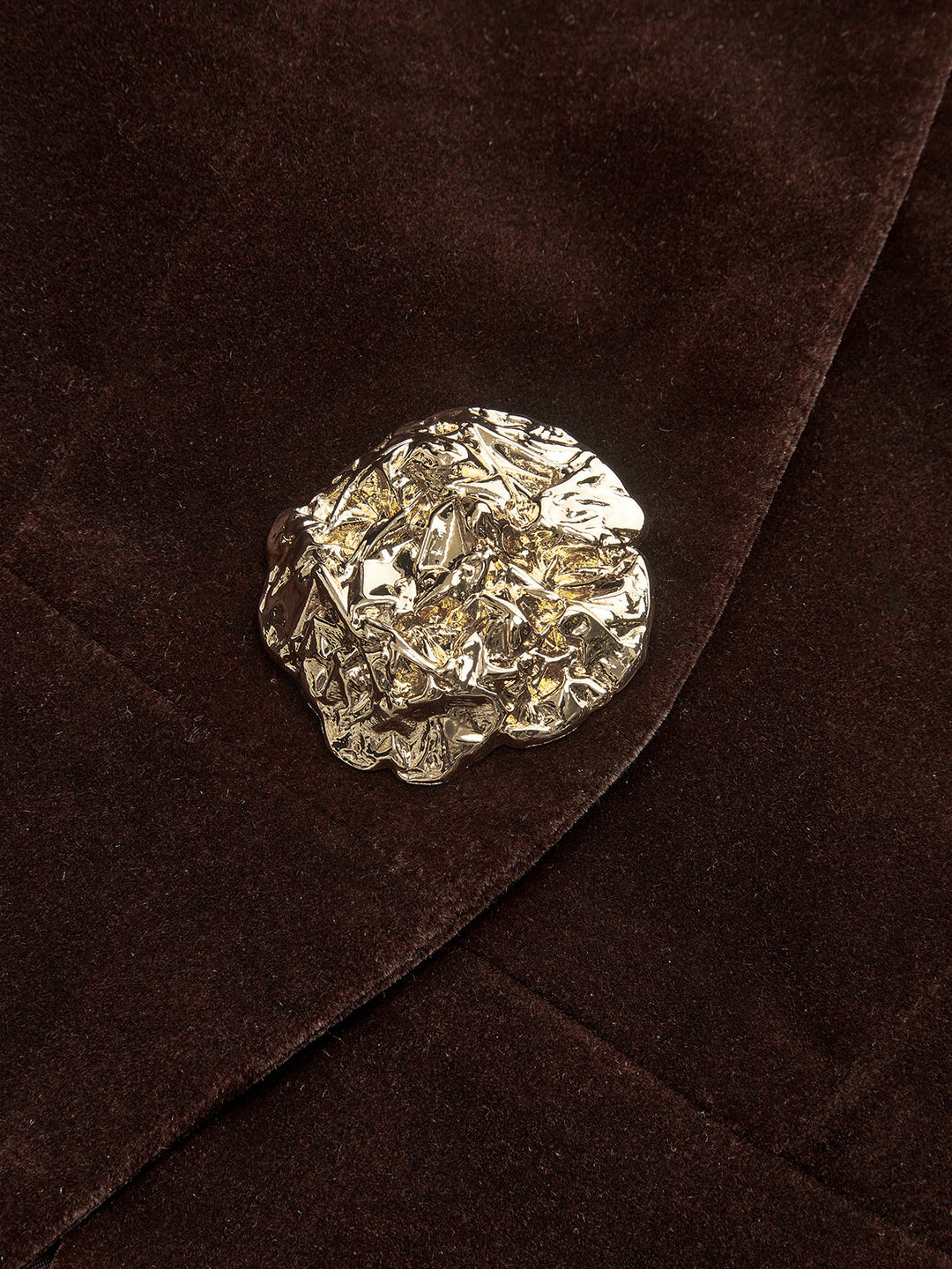 Macro of the sculpted gold flower button on the brown velvet lapel edge
