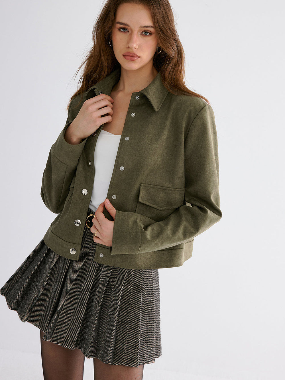 Olive suede jacket worn open over a white top with a grey pleated mini skirt