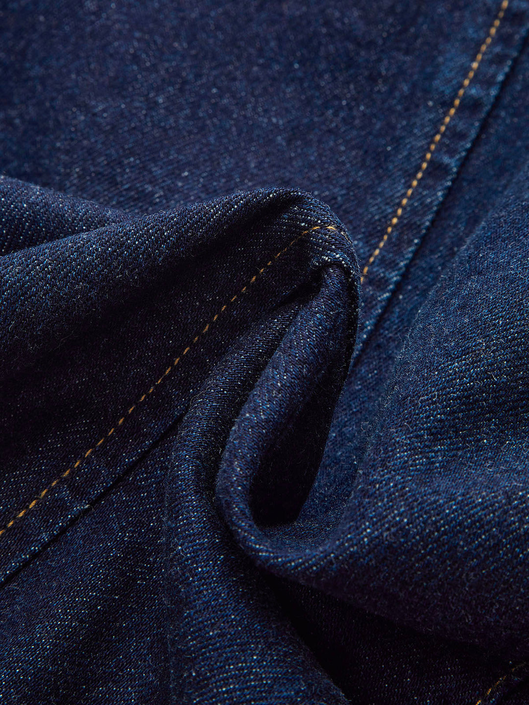 Macro of dark indigo denim with contrast gold topstitching on a women's fitted jacket