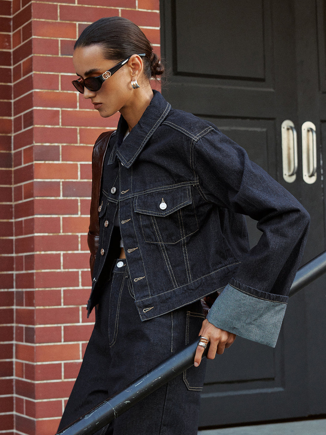 Women's cropped raw denim trucker jacket with contrast stitching, front view in the street