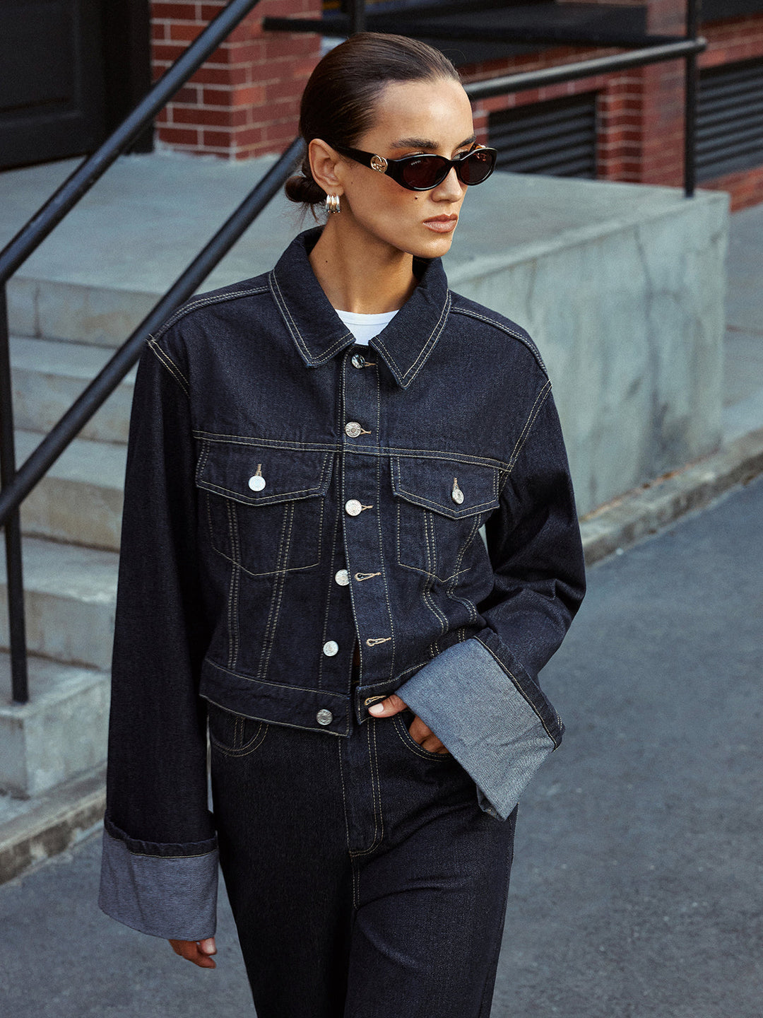 Model standing with the blue denim jacket open over a white crop top